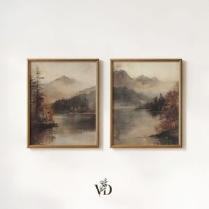 May include: Two rectangular framed wall art prints featuring muted landscape paintings of misty mountains, calm lakes, and autumn-toned trees. The artwork displays a soft, hazy atmosphere with earthy brown, grey, and orange hues in thin gold frames.