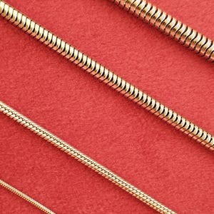 May include: Four gold snake chains of different sizes on a red background.