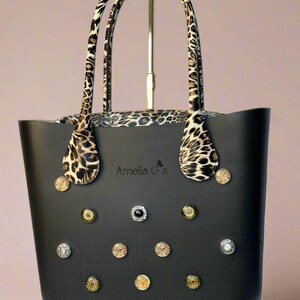 May include: Black tote bag with leopard print handles and decorative buttons. The bag has the text "Amelia G's" on the front.