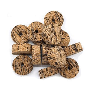 Puede incluir: Una colección de piezas de corcho natural en varias formas, incluyendo discos circulares con agujeros centrales y bloques rectangulares. El corcho tiene un color marrón claro con patrones lineales marrón oscuro y una superficie texturizada.