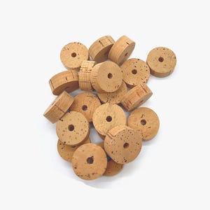 May include: A pile of natural cork rings with a hole in the center. The rings are light brown and have a rough texture.