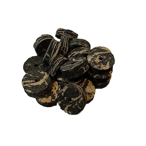 May include: A collection of black and tan cork bottle stoppers with a marbled design. The stoppers are round with a hole in the center, and some are rectangular. The corks are stacked together on a white background.