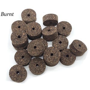 May include: A pile of 20 burnt cork guitar tuning pegs. The pegs are round with a hole in the center. The pegs are a dark brown color.