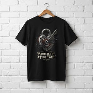 Puede incluir: Camiseta negra con un diseño de cerradura en forma de corazón y una llave, con el texto "PROTECTED BY A PLOT TWIST". El diseño presenta detalles plateados y marrones, creando un estilo vintage.