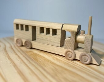 May include: A wooden toy train with a single car and a locomotive. The train is made of natural wood and has a simple design. The train is sitting on a wooden surface.