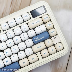 Puede incluir: Un teclado blanco con teclas azules y blancas. El teclado tiene una tecla azul que dice "Keep Refrigerated".