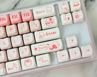Puede incluir: Un teclado mecánico personalizado con teclas rosas y blancas. Las teclas presentan ilustraciones de gatos y texto como "Back", "Enter" y "Shift". El teclado tiene un marco rosa y una variedad de teclas de función.
