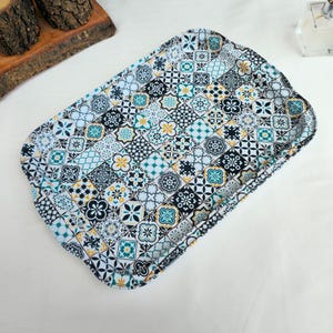 Könnte beinhalten: Rechteckiges Serviertablett mit farbenfrohem Fliesenmuster. Das Tablett weist ein sich wiederholendes Design aus geometrischen Formen in Türkis, Schwarz, Weiß und Gelb auf. Das Tablett hat abgerundete Ecken und einen leicht erhöhten Rand.