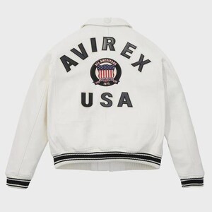 May include: A cream-coloured jacket with black and white striped cuffs and collar. The back displays the word "AVIREX" above a circular emblem with the American flag and the word "USA" below.