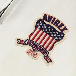 May include: A white leather jacket with a patch displaying the word "AVIREX" in red, a blue field of stars, and red and white stripes. The patch also includes the text "N.Y. ESTABLISHED 1975."