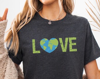 Puede incluir: Una camiseta gris oscuro con un gráfico desgastado que dice "LOVE" con un globo terráqueo verde y azul en forma de corazón.