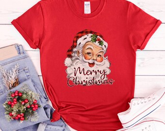 May include: Red t-shirt with a vintage illustration of Santa Claus wearing a red and black plaid hat. The text "Merry Christmas" is printed below the illustration.