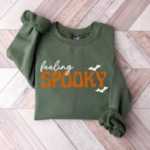 This image features the Feeling Spooky design for the military green sweatshirt.