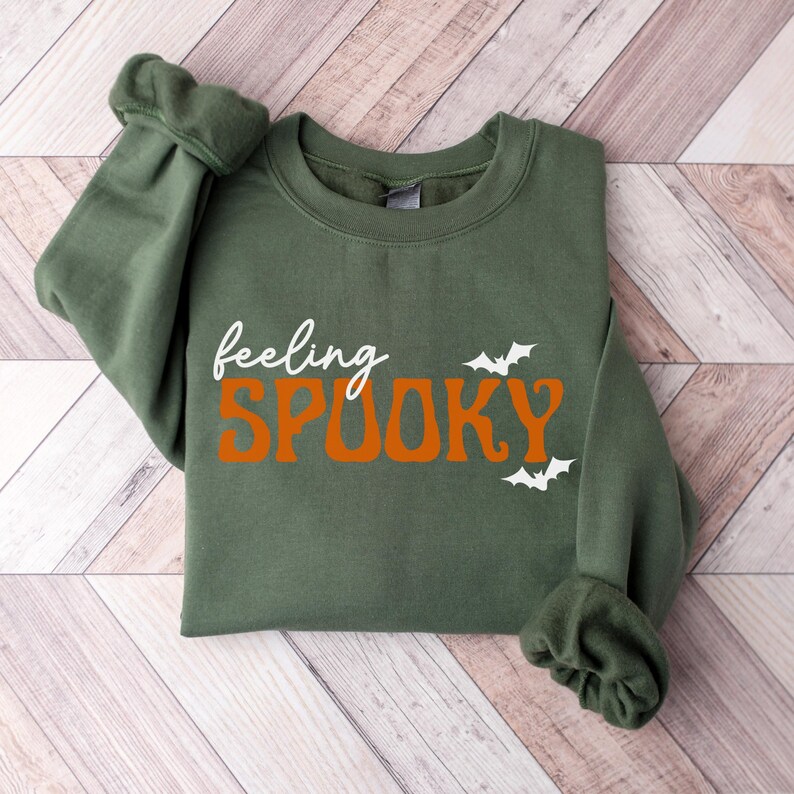 This image features the Feeling Spooky design for the military green sweatshirt.
