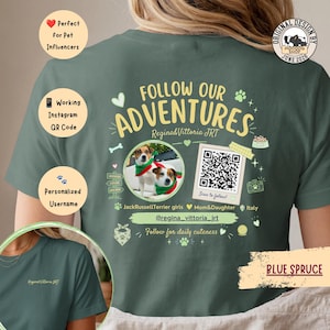 Può includere: Una t-shirt color abete blu con una grafica sul retro che riporta il testo FOLLOW OUR ADVENTURES, Regina&Vittoria JRT e @regina_vittoria_jrt. Il design include una foto circolare di due Jack Russell Terrier, un codice QR e icone di impronte.