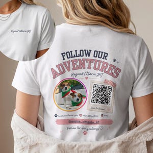 Può includere: Una t-shirt bianca con una grafica sul retro che riporta il testo FOLLOW OUR ADVENTURES, Regina&Vittoria JRT e una foto circolare di due Jack Russell Terrier con sciarpe verdi. Include un codice QR, un handle social e icone a forma di zampa.