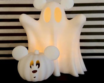May include: White Halloween decorations featuring a ghost and a pumpkin, both with mouse-ear designs. The ghost has glowing orange eyes, and the pumpkin has a carved face. The background is black and white striped.