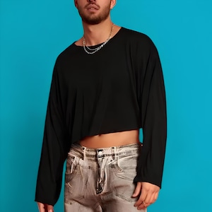May include: A black long-sleeved cropped shirt with a scoop neck and a silver chain necklace. The shirt is worn over a pair of light gray jeans.