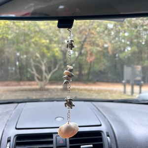 May include: A car rearview mirror with a hanging ornament featuring a seashell and multiple turtle charms on a silver chain.