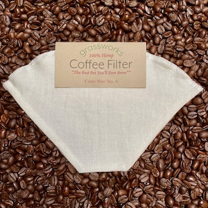 May include: A white hemp coffee filter, cone size 6, on a bed of coffee beans. The filter is made from 100% hemp and is reusable. The text on the label reads "grassworks 100% Hemp Coffee Filter "The Best Pot You'll Ever Brew" Cone Size No. 6"