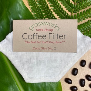 Puede incluir: Un filtro de café de cáñamo blanco con el texto "grassworks 100% Hemp Coffee Filter "The Best Pot You'll Ever Brew"™ Cone Size No. 2" impreso en una etiqueta marrón.