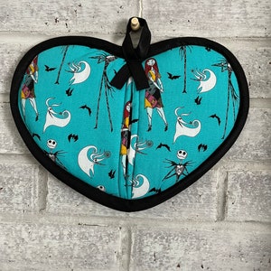 May include: A heart-shaped teal blue oven mitt with a black trim and a black ribbon. The mitt features a repeating pattern of Sally and Jack Skellington from the Nightmare Before Christmas.