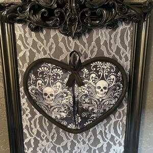 May include: A black ornate frame with a white lace background and a black heart-shaped pot holder with a white and black skull design.