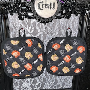 May include: A pair of black quilted oven mitts with a repeating pattern of Chucky and Tiffany from the Child's Play horror movie franchise. The mitts have a black border and a white "Chucky" text.