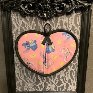 May include: A pink heart-shaped oven mitt with a black trim and a pattern of blue Stitch characters from Lilo & Stitch eating bananas.