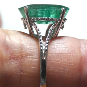 May include: A silver ring featuring a large, emerald-cut green gemstone. The ring has an ornate, openwork design around the gem and a detailed band. The gemstone is a vibrant green color, and the ring is set against a light background.