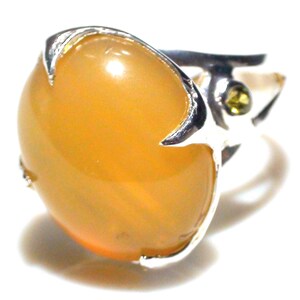May include: A silver ring featuring a large, oval, amber-colored gemstone. The gemstone is set in a silver band with claw-like prongs. A small, round, green gemstone accents the band.