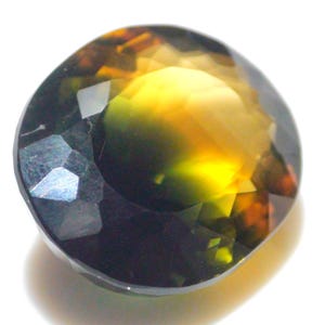 May include: A round, faceted gemstone displaying a blend of colours: yellow, orange, and dark green. The polished surface and intricate, geometric cut create a sparkling effect as light reflects off the facets. A beautiful piece of jewellery.