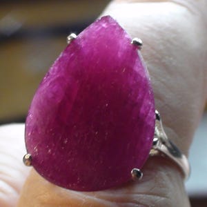 Puede incluir: Un anillo con una gran piedra preciosa de rubí rosa oscuro en forma de pera engastada en plata.