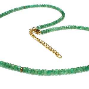 May include: A necklace composed of small, faceted green emerald beads strung together. The strand is accented with evenly spaced, thin gold-toned metal rings. It features a gold-toned metal lobster claw clasp and an adjustable chain extender.