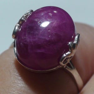 Könnte beinhalten: Ein silberner Ring mit einem großen, ovalen, violetten Edelstein. Der Ring hat ein zartes, verziertes Design.