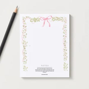May include: A white notepad with a pink bow and floral border, and a black pencil with a gold ferrule. The notepad has the word "NOTES" and a Bible verse at the bottom. The notepad is designed for taking notes.