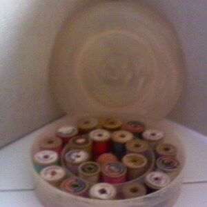 May include: A white plastic container filled with spools of colorful thread. The spools are arranged in a circular pattern and are of various sizes and colors.