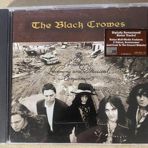 May include: CD case for "The Southern Harmony and Musical Companion" by The Black Crowes. The cover features the band members in black and white, with the album title and band name in brown and gold. A sticker indicates it's digitally remastered.