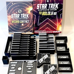 May include: A Star Trek Captain's Chair board game set including two game boxes, black plastic card organizers, and labeled trays. The trays feature text such as Captain, Glory, Ship, Latinum, Dilithium, Exhaustion, and various character names.