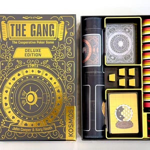 May include: The Gang Deluxe Edition cooperative poker game box and open interior. The black box features gold foil text and a vault graphic. Inside are a rolled black playmat, a deck of cards, yellow tokens, and a stack of red, yellow, and white chips.