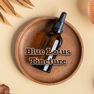 May include: A brown glass bottle with a black dropper sits on a wooden plate. The bottle contains a liquid and is labeled "Blue Lotus Tincture" in a decorative font. The background is a neutral beige color.