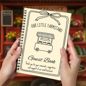 May include: A spiral-bound guest book with a cream-colored cover. The cover features the text "OUR LITTLE FARMSTAND" above a drawing of a farm stand and the words "Guest Book". The bottom of the cover reads "Thank you for your comments, suggestions and support of our small business!"