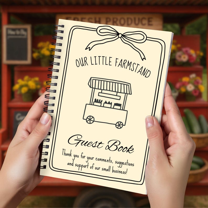 May include: A spiral-bound guest book with a cream-colored cover. The cover features the text "OUR LITTLE FARMSTAND" above a drawing of a farm stand and the words "Guest Book". The bottom of the cover reads "Thank you for your comments, suggestions and support of our small business!"