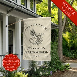 May include: A cream-colored garden flag with black text and a graphic of bread and wheat. The text reads "Barb's Baked Goods Homemade Sourdough Bread".