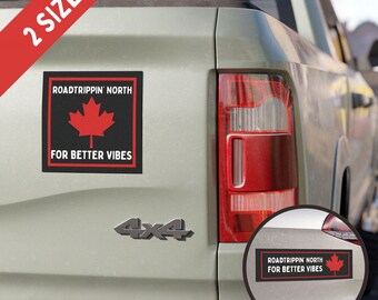 Könnte beinhalten: Ein schwarzer und roter Automagnet mit dem Text "Roadtrippin' North For Better Vibes" und einem roten Ahornblatt. Der Magnet ist an der Rückseite eines grauen Pick-up-Trucks befestigt.