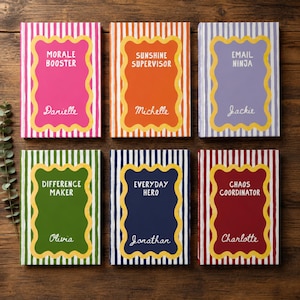 May include: Six rectangular notebooks with striped covers and scalloped central frames. The covers feature the text: Morale Booster Danielle, Sunshine Supervisor Michelle, Email Ninja Jackie, Difference Maker Olivia, Everyday Hero Jonathan, and Chaos Coordinator Charlotte.