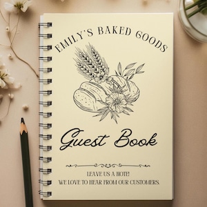 May include: Spiral-bound guest book with the text "EMILY'S BAKED GOODS" and "Guest Book" in black script. The cover features a line drawing of wheat, bread, and flowers. The bottom of the cover reads "LEAVE US A NOTE! WE LOVE TO HEAR FROM OUR CUSTOMERS."