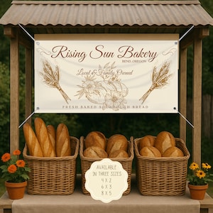 May include: A bakery stand with a banner reading "Rising Sun Bakery, Bend, Oregon, Local & Family Owned, Fresh Baked Sourdough Bread." Baskets of bread are displayed below the banner. The sign also states the available sizes: 4x2, 6x3, and 8x5.