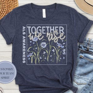 May include: A navy blue t-shirt with a floral design and the text "Together we rise" and "ALS Awareness".