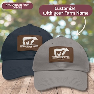 May include: Two baseball caps with a brown leather patch featuring a cow and a chicken silhouette. The text on the patch reads "Henderson Farm Since 2003". One cap is navy blue and the other is grey.